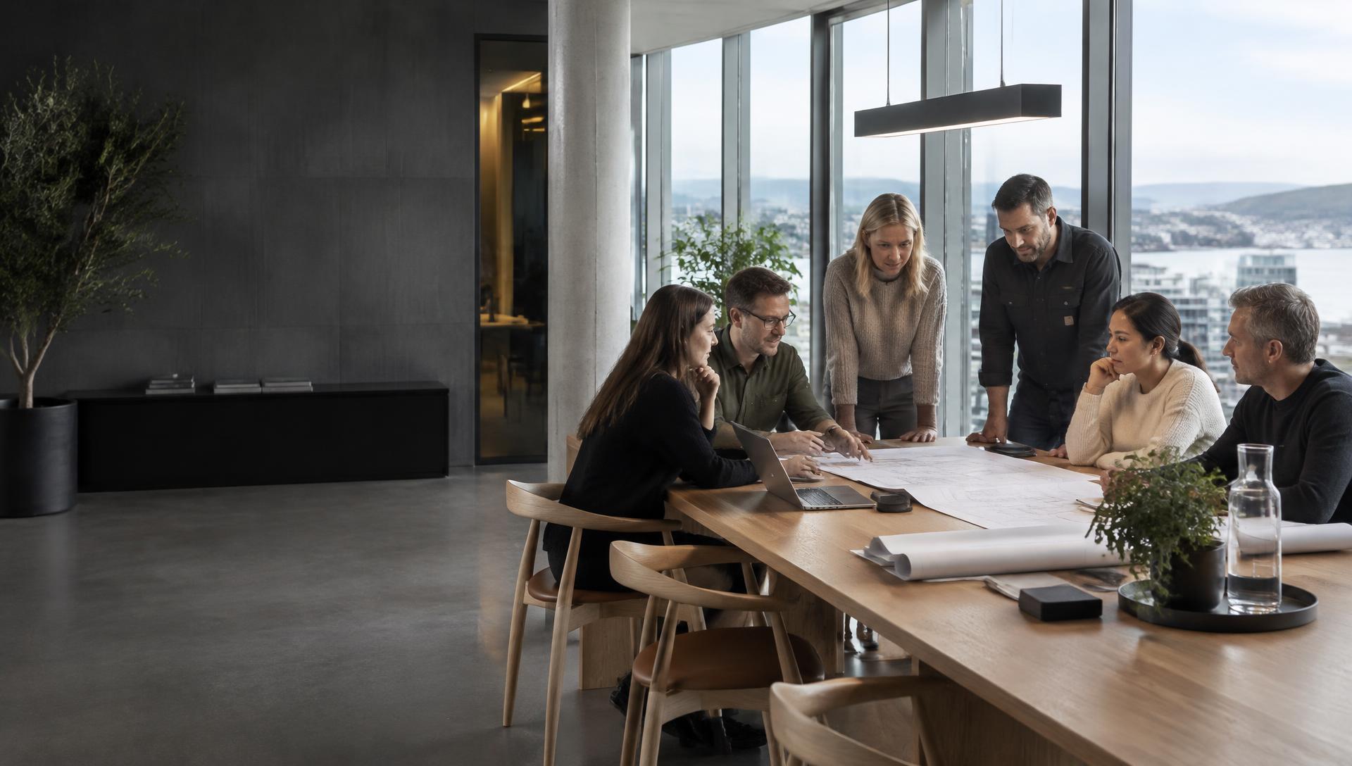 Kollegaer fra ulike avdelinger samarbeider rundt et bord på en moderne norsk arbeidsplass